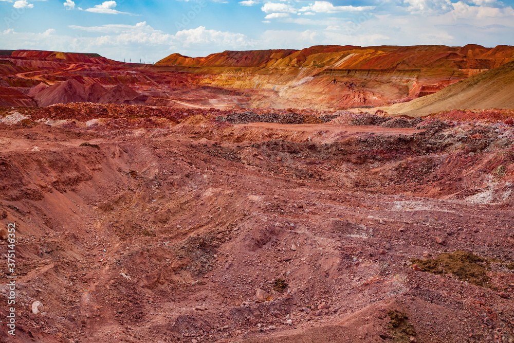Aluminium ore quarry. Bauxite clay open-cut mining. Color heaps of empty rocks. Blue sky with clouds. Panorama view.