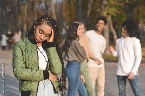 Upset Teen Black Girl With Friends Gossiping In Background photo