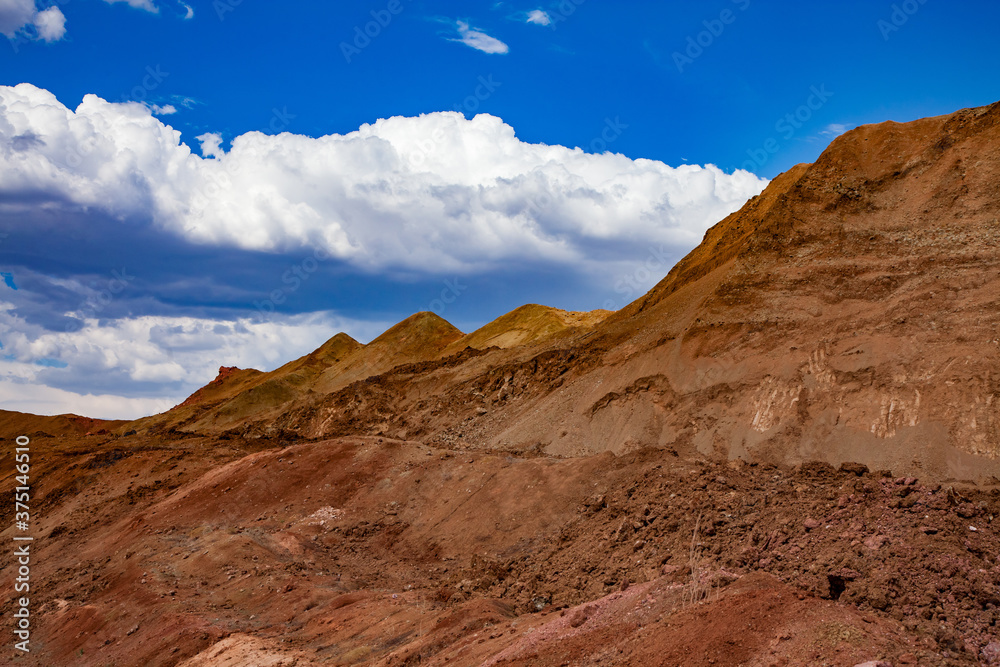 Bauxite open cast (open cut) mining. Color aluminium ore quarry. Big yellow piles of empty rocks. (Slag heaps). On blue sky with clouds.