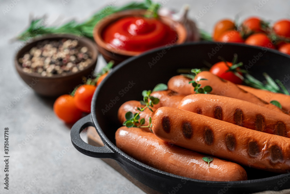 Roasted sausages in cast-iron frying pan over concrete background.