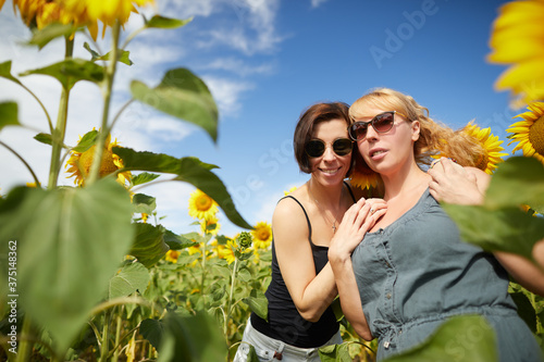 Two adult caucasian sisters together in sunflowers field in summertime.