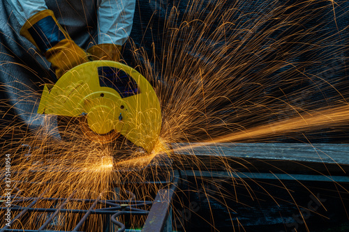 Hands of man with glove using electric steel cutter machine while working at workshop. Male cutting steel with sparks flying. Hard work in factory or garage industry in construction site concept.