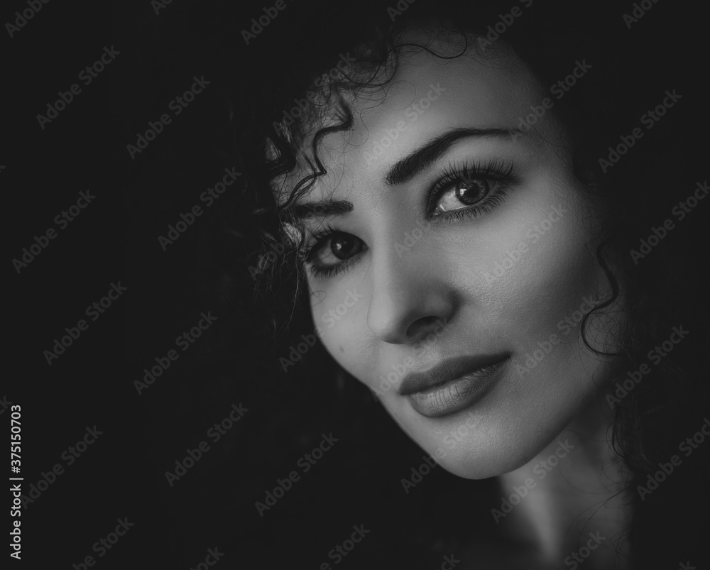 Beautiful young woman with curly hair looking sexy with half shadow on the face. Closeup portrait. Black and white Photography. 