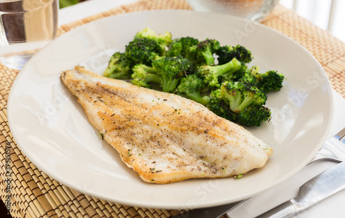 fried fillet of sea bass with garnish of broccoli on black warm stone plate