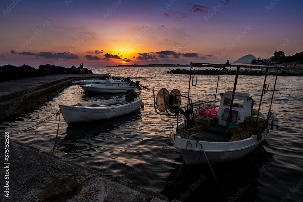 Stunning sunset on the adriatic sea with fisherman boats in the harbor on the foreground and the mountain on the background. Greece 2020