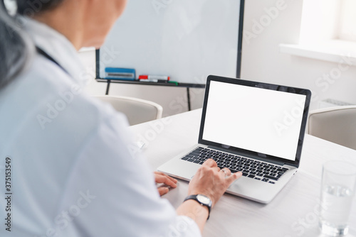 Female doctor using laptop with mockup on screen for medical work at modern hospital office
