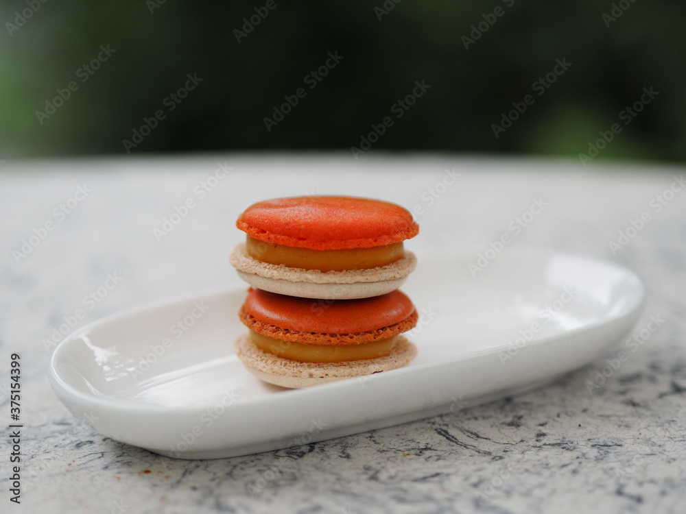Macaron orange color in white plate shape ellipse, Dessert snacks Afternoon on marble table