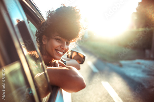 Beautiful curly hair woman enjoying the breeze, looking out of the window's car while having a road trip photo