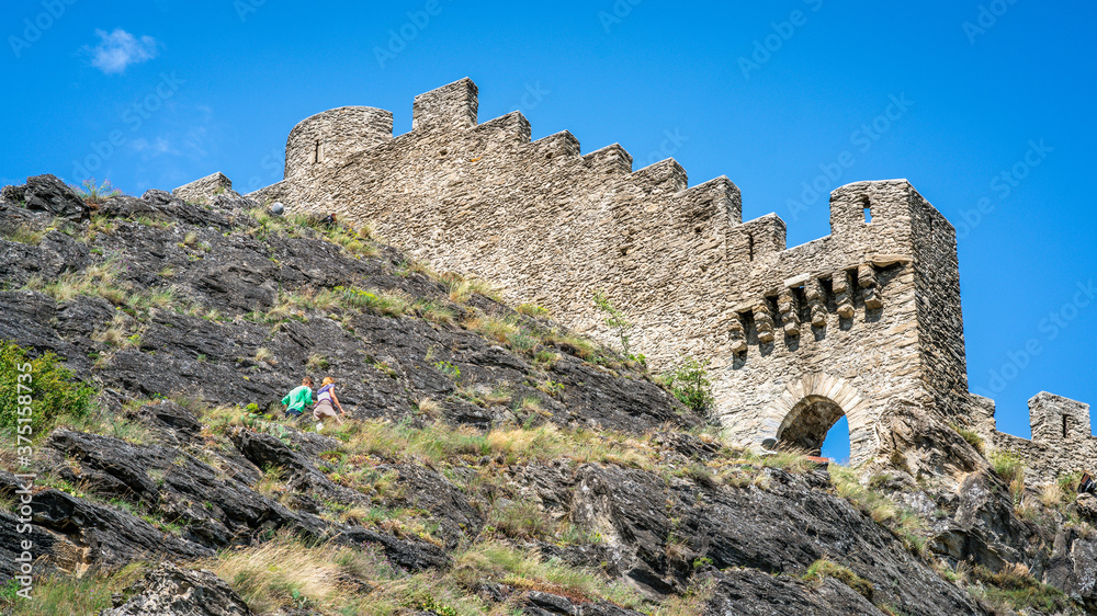 Entrance and wall of the ruins of Tourbillon castle with tourist going up the hill in Sion Switzerland