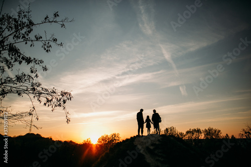  family with daughter look at the sunset in autumn  their silhouettes stand on a slide in the park