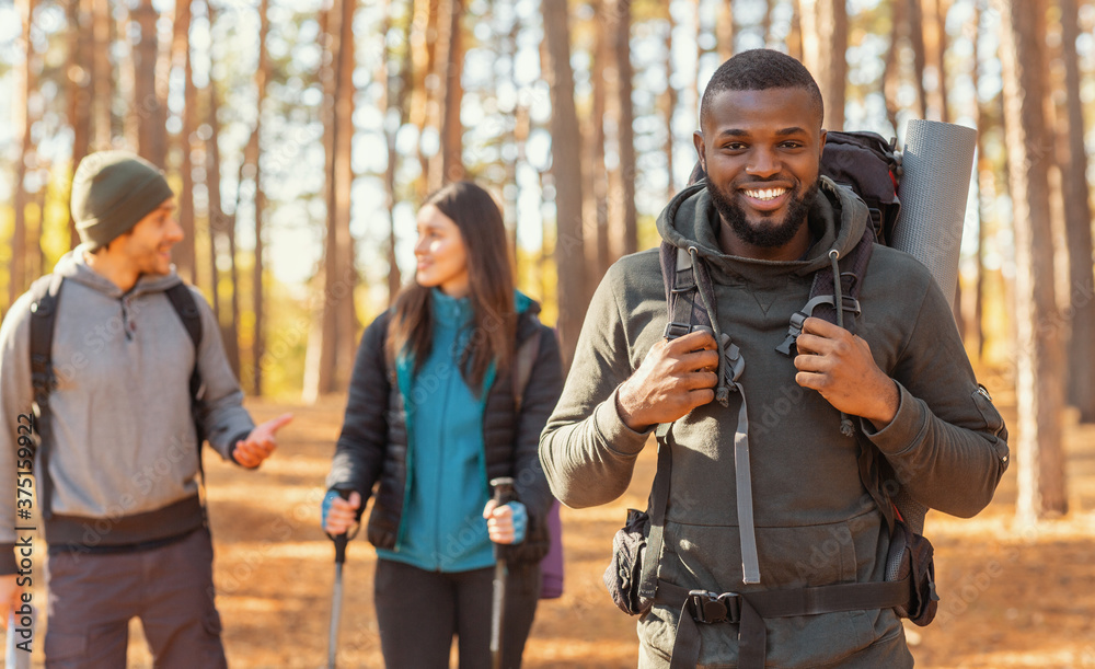 Fototapeta premium Happy black guy hiking with friends by countryside