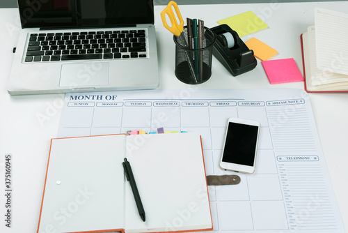 Book,laptop,pen,steel pen's box and scissors are on the white table in room or office,knowledge for search information and prepare short note shopping on line. photo