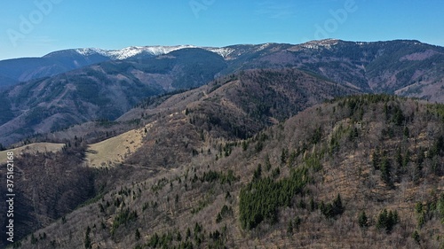 Aerial view of naked and forested hills under High Tatra mountains during dry winter without snow. Mixed forests contains mostly spruce trees and various naked broadleaf trees.