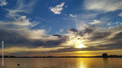 Day to night time lapse sun moving in clouds with reflection in calm lake photo