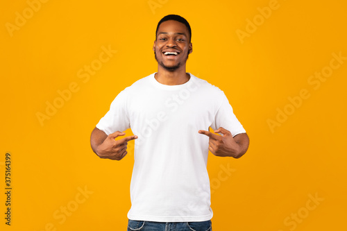 African Man Pointing At Himself Standing In Studio, Yellow Background