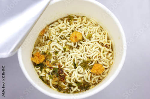 instant noodles, noodle soup in a cup, view from above. Instant noodles are sold in a precooked and dried noodle block, with flavoring powder and/or seasoning oil.