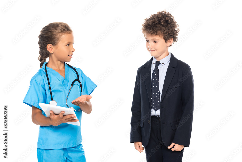 child in costume of doctor pointing with hand at digital tablet near curly boy in formal wear isolated on white child in costume of doctor pointing with hand at digital tablet near curly boy in formal wear isolated on white