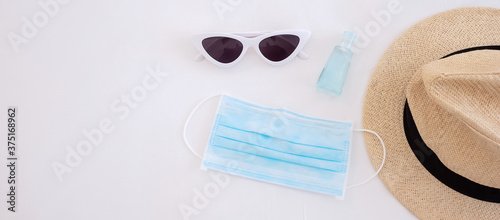 Travel under Covid-19 and new normal concepts. medical face mask, hand gel sanitizer, sunglasses and beach hat on white bed, prevent coronavirus or Corona Virus Disease
