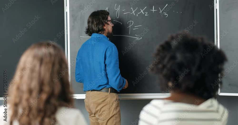 Caucasian man teacher at school writing formulas and mathematics laws on blackboard. School concept. Male lecturer in glasses explaining math laws to pupils. Educational concept. Caucasian man teacher at school writing formulas and mathematics laws on blackboard. School concept. Male lecturer in glasses explaining math laws to pupils. Educational concept.