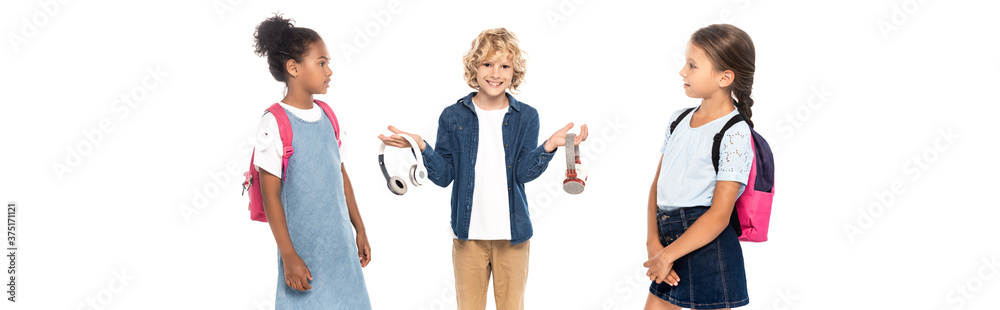 panoramic shot of blonde schoolboy holding wireless headphones near multicultural schoolgirls isolated on white panoramic shot of blonde schoolboy holding wireless headphones near multicultural schoolgirls isolated on white