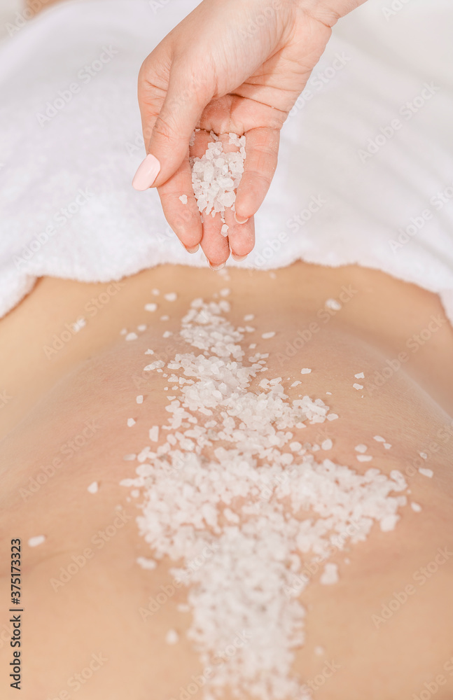 Fototapeta premium Spa scrub massage. Hands sprinkle salt on back of girl