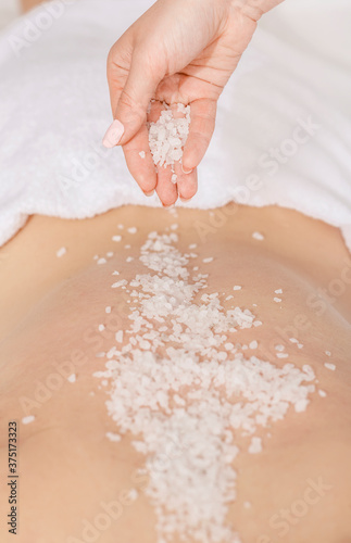 Spa scrub massage. Hands sprinkle salt on back of girl