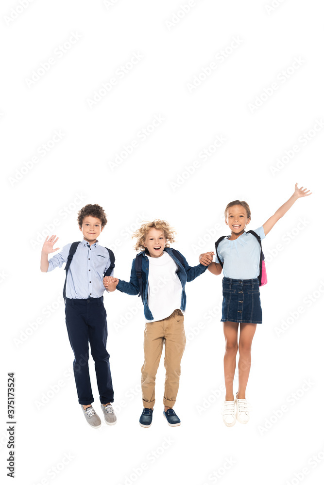 curly schoolboys holding hands with schoolgirl and jumping isolated on white