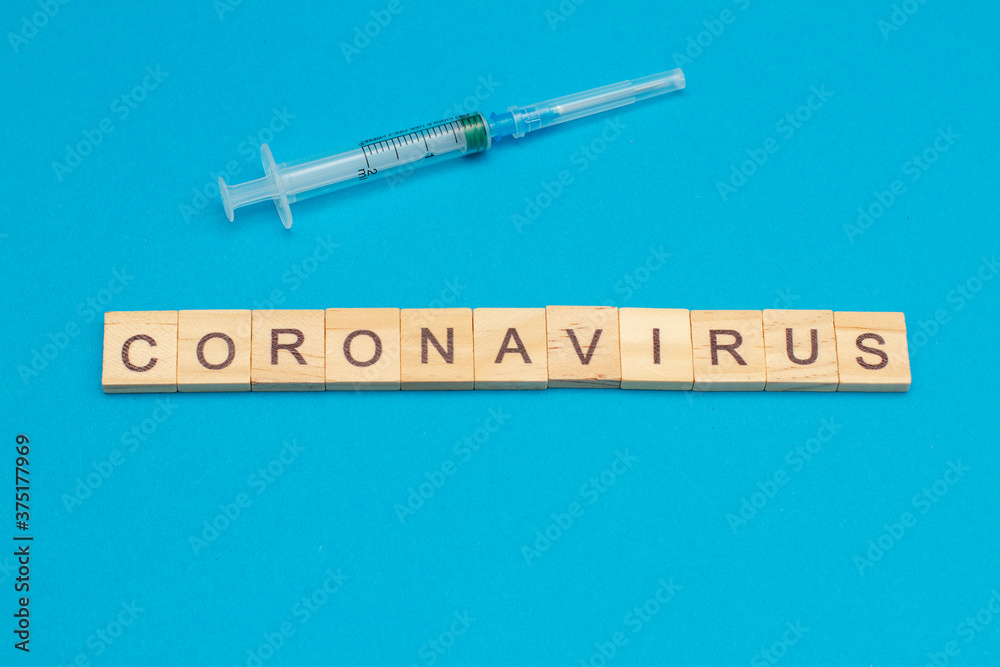 Word CORONAVIRUS made from wooden cubes and and surgical syringe on blue background Word CORONAVIRUS made from wooden cubes and and surgical syringe on blue background