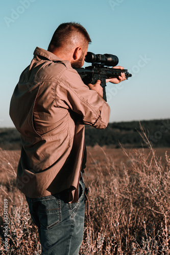 A hunter with a weapon on the hunt against the backdrop of a beautiful summer landscape. Shooter sighting in the target. The Bearded man is on the hunt. Soft focus