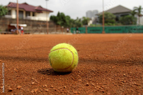 Tennis ball on a tennis clay court. Red clay tennis court. Sand on a tennis court. Close up of tennis ball on clay court © Arief Bagus