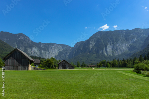 Rural wooden houses in the mountains. View of green summer landscape. Meadow with flowers. Mountain scenery. Hiking active day. Rural path in the countryside. Fresh air healthy lifestyle.Alpine living