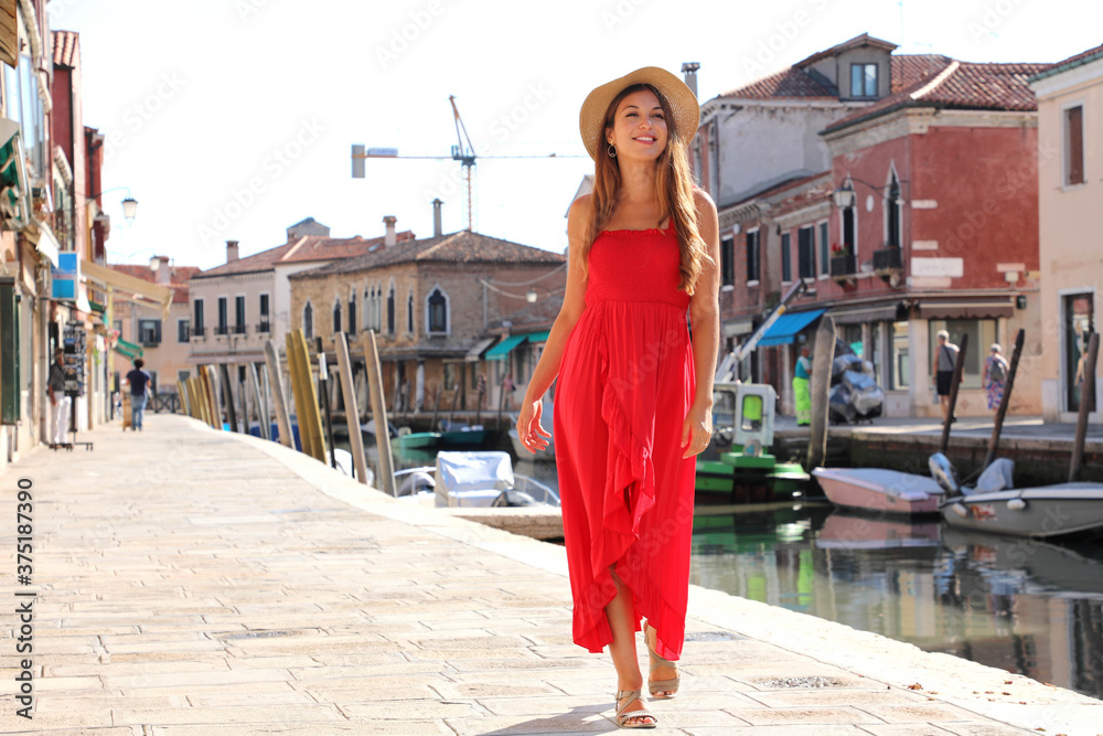 Elegant woman in red long dress walking in the old town of Murano, Venice, Italy