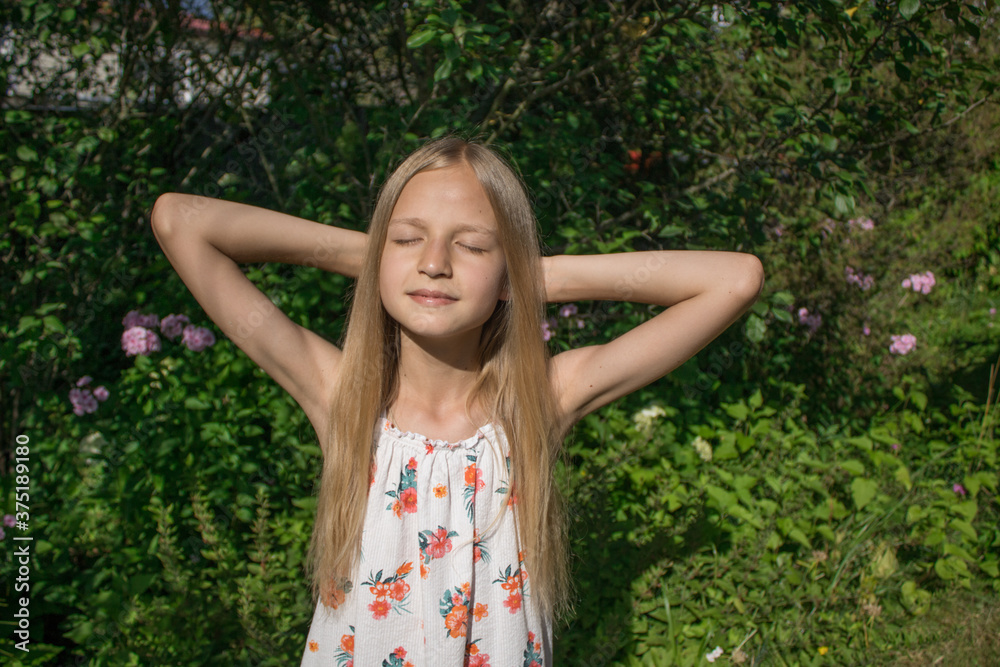 Girl with golden hair is sunbathing under the warm summer sun against a background of bright green foliage. The concept of happy childhood, sunny summer, autumn, pleasant memories and emotions Girl with golden hair is sunbathing under the warm summer sun against a background of bright green foliage. The concept of happy childhood, sunny summer, autumn, pleasant memories and emotions