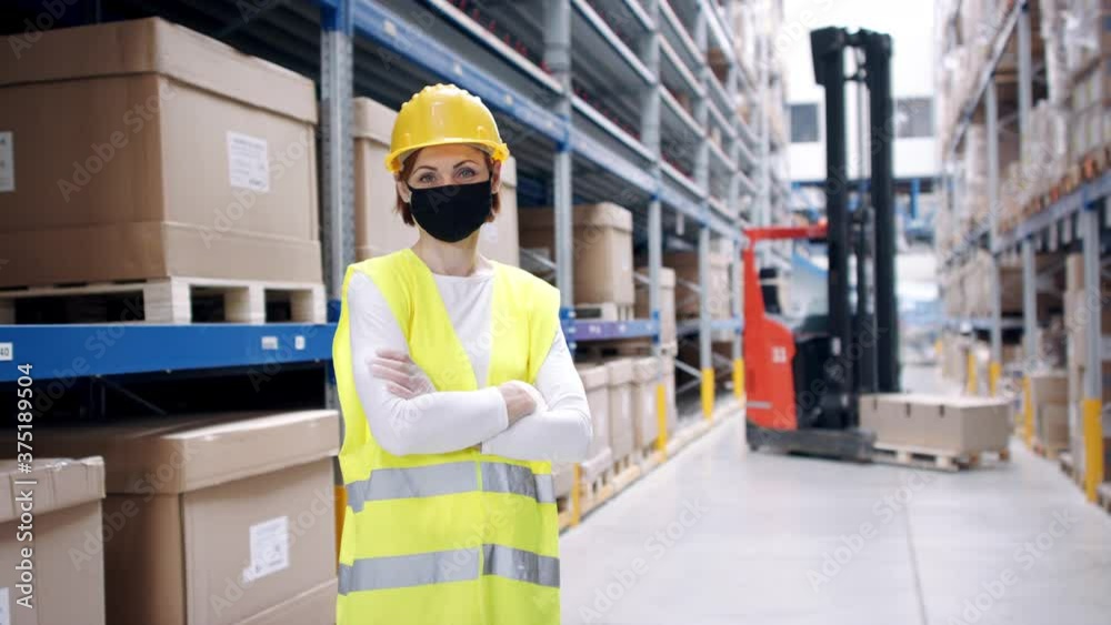 Portrait of a young woman worker with gloves and face mask standing in warehouse.