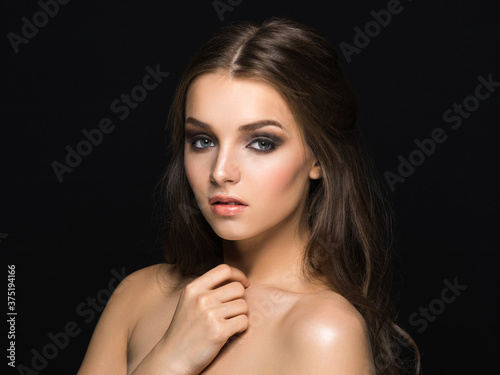 Young amazing girl with long wavy hair and sophisticated heavy makeup looking at camera isolated on black.