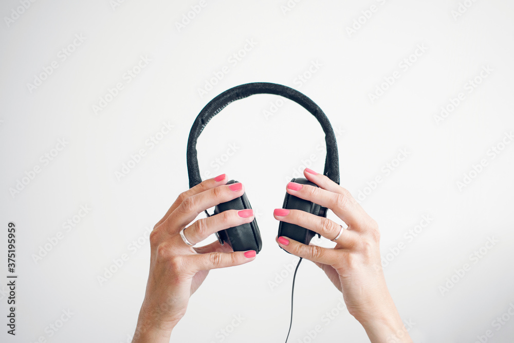 Two female hands holding up headphones in front of a white wall. Two female hands holding up headphones in front of a white wall.