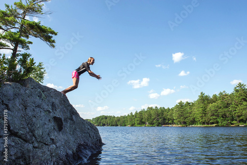 Girl leans, just about to jump off a rock into a lake