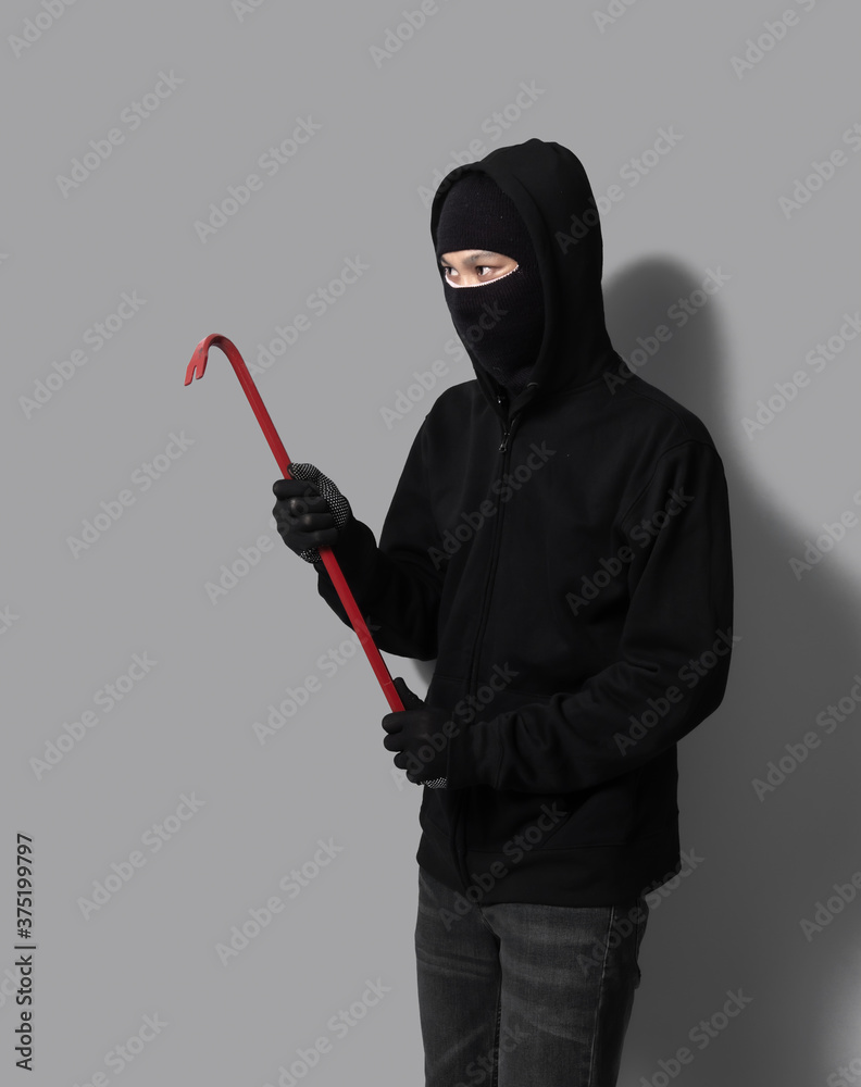 Burglar concept,Masked thief in balaclava with crowbar on gray background Burglar concept,Masked thief in balaclava with crowbar on gray background