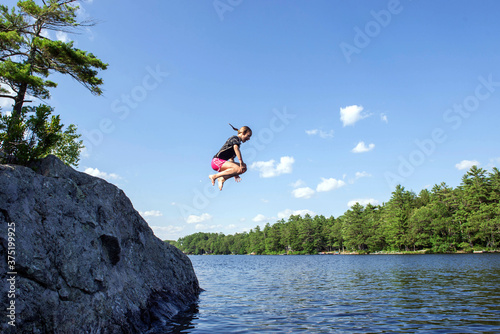 Girl does a cannonball jump off a rock into the lake