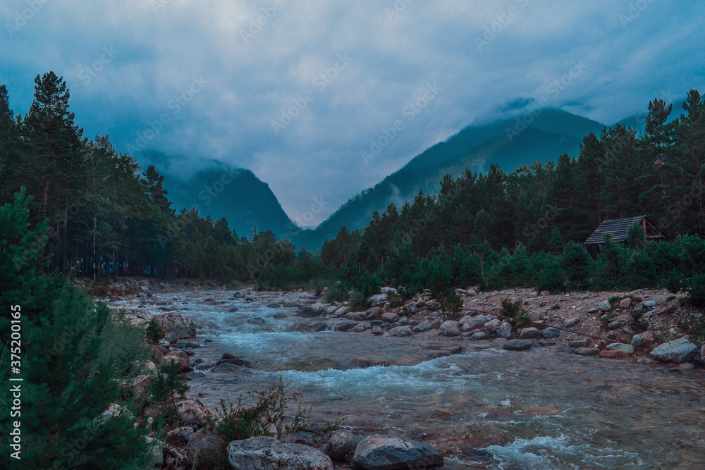 A mountainous clean blue seething river flows between stones rocks and high mountains covered with green morning forest A mountainous clean blue seething river flows between stones rocks and high mountains covered with green morning forest
