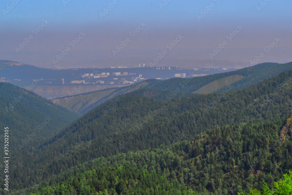 Landscape with green trees mountains and a view of a polluted gray city in smoke, dirty air