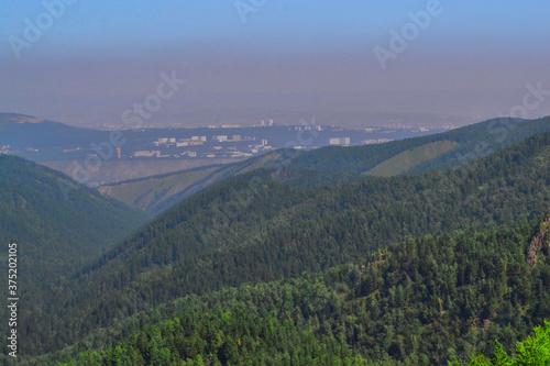 Landscape with green trees mountains and a view of a polluted gray city in smoke, dirty air