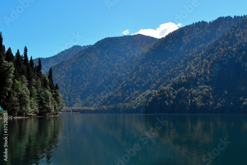 Beautiful blue clear emerald Lake Ritsa in Abkhazia glowing in the sun near the middle of high green trees mountains