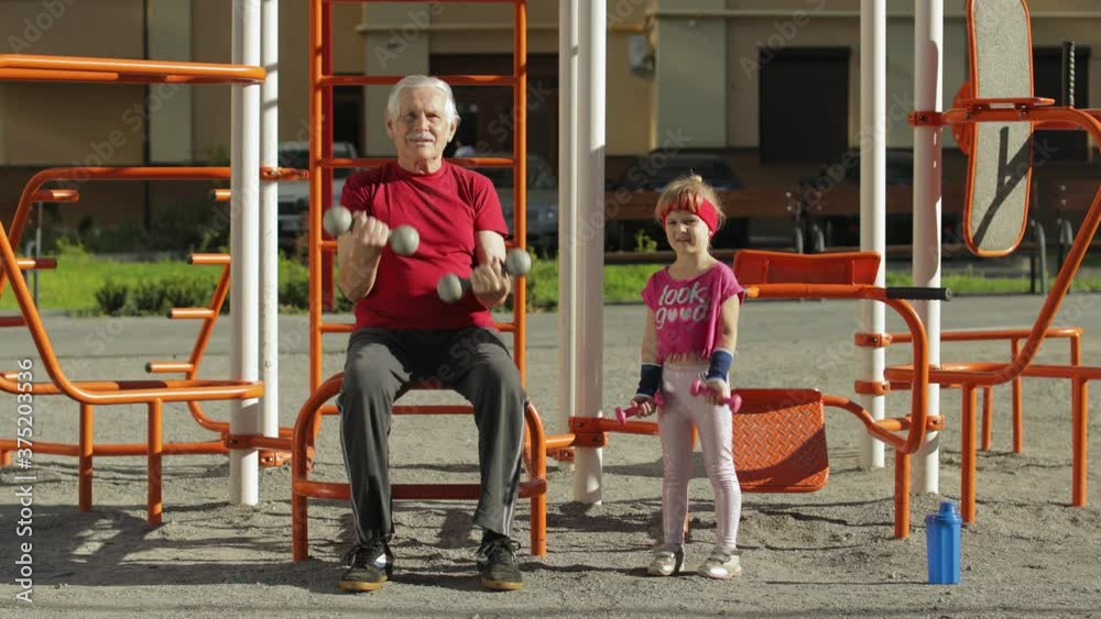Granddaughter and grandfather doing fitness exercises with dumbbells. Senior man with child kid girl Granddaughter and grandfather doing fitness exercises with dumbbells. Senior man with child kid girl