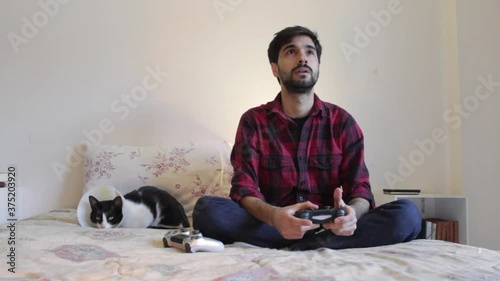 Handsome millenial single man plays videogames in bed with his cat and celebrates wining during quarantine photo