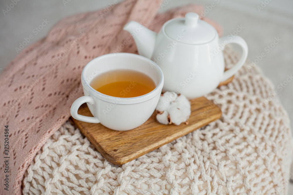 A mug of hot tea, a teapot, a wooden stand on an ottoman. Cozy autumn. Winter breakfast. Cotton. A mug of hot tea, a teapot, a wooden stand on an ottoman. Cozy autumn. Winter breakfast. Cotton.