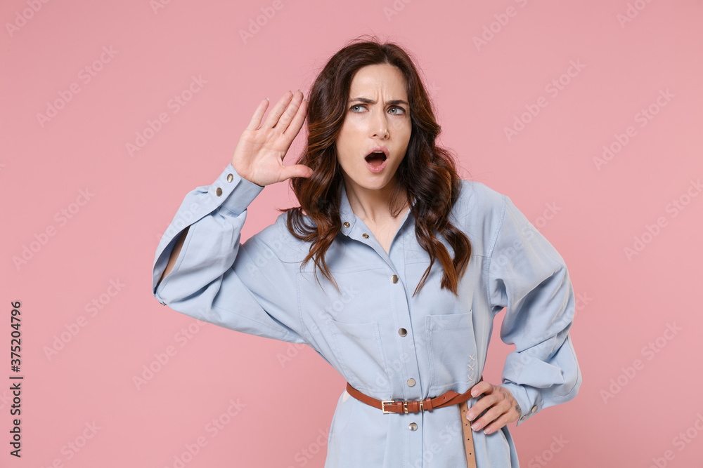 Shocked curious young brunette woman 20s wearing casual blue shirt dress posing try to hear you overhear listening intently looking aside isolated on pastel pink colour background, studio portrait. Shocked curious young brunette woman 20s wearing casual blue shirt dress posing try to hear you overhear listening intently looking aside isolated on pastel pink colour background, studio portrait.