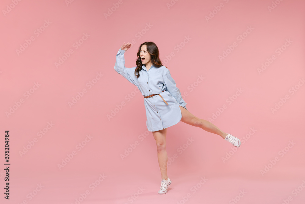 Full length portrait excited young brunette woman 20s wearing casual blue shirt dress holding hand at forehead looking far away distance rising hand isolated on pastel pink colour background studio. Full length portrait excited young brunette woman 20s wearing casual blue shirt dress holding hand at forehead looking far away distance rising hand isolated on pastel pink colour background studio.
