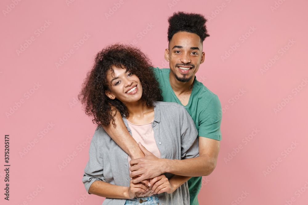 Smiling cheerful funny young african american couple two friends guy girl in gray green casual clothes posing hugging looking camera isolated on pastel pink color wall background studio portrait. Smiling cheerful funny young african american couple two friends guy girl in gray green casual clothes posing hugging looking camera isolated on pastel pink color wall background studio portrait.