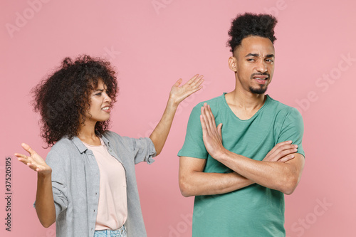 Irritated displeased young african american couple two friends guy girl in gray green casual clothes posing spreading hands speaking swearing isolated on pastel pink color background studio portrait.